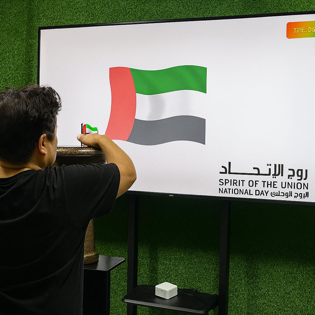 Guest playing Drum-to-Reveal interactive game at a Dubai event, beating the drum to reveal a hidden image on a large screen, designed for exhibitions and activations.